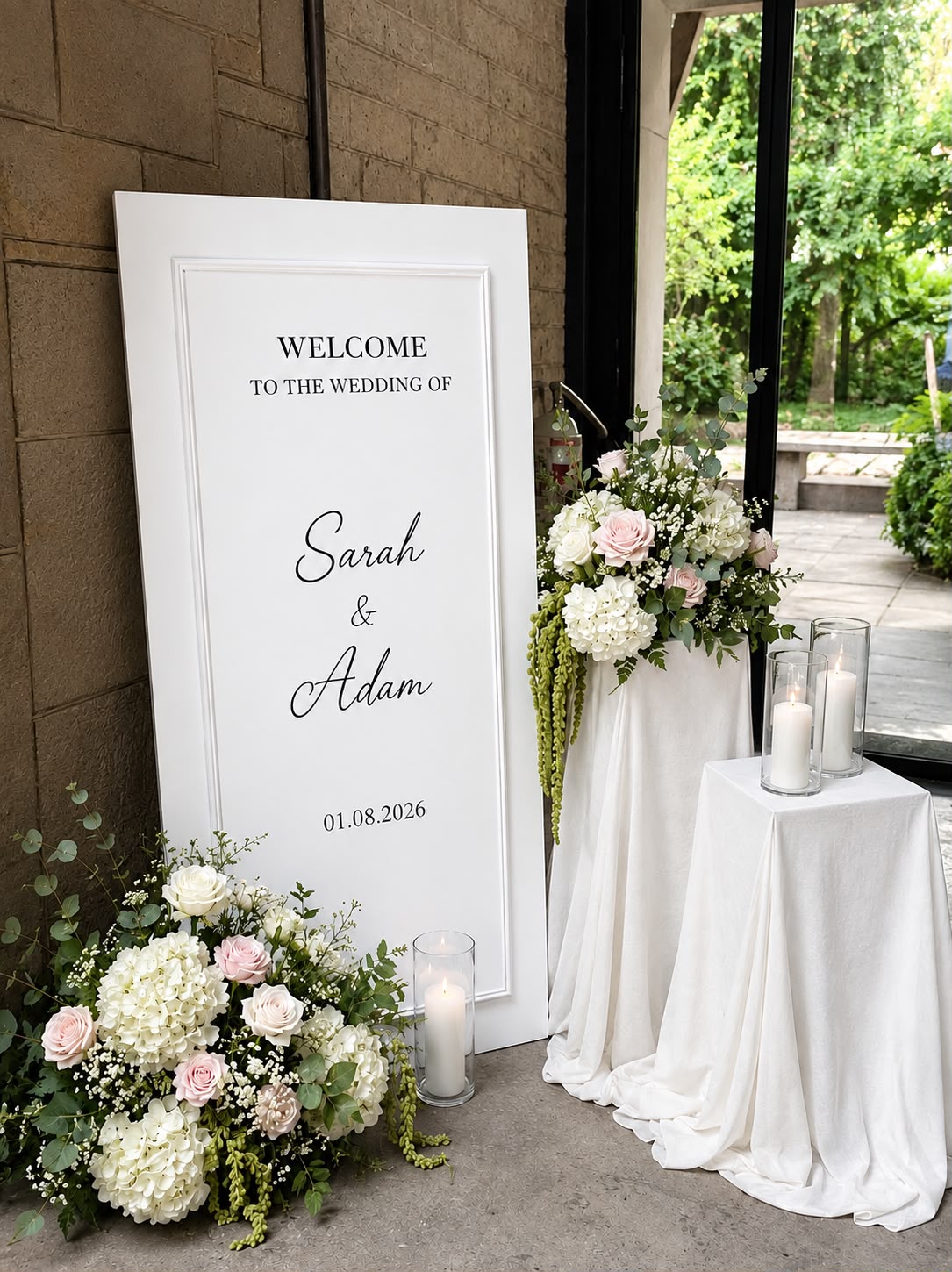 Welkomstbord bruiloft met witte en roze bloemen en kaarsen