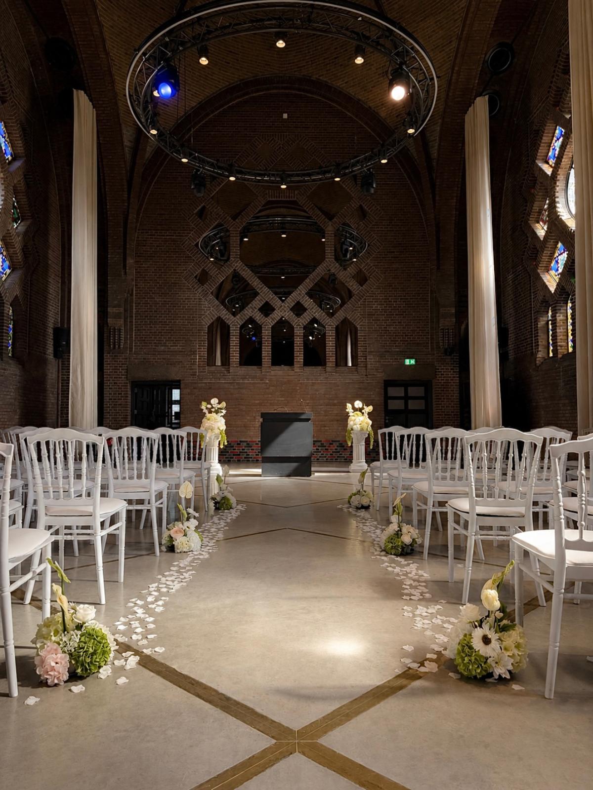 Gangpad met rozenblaadjes, bloemstukken en witte stoelen in een bakstenen kerkzaal