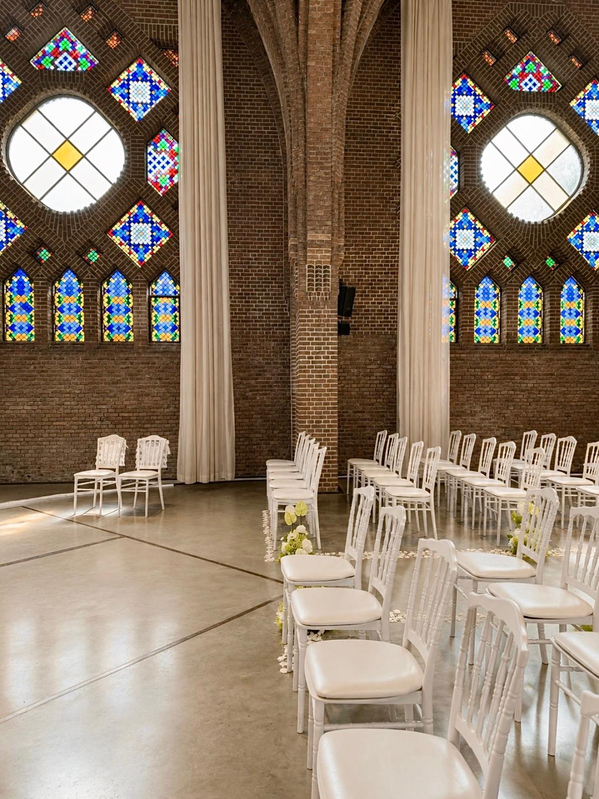 Ceremonieopstelling met witte stoelen onder glas-in-loodramen