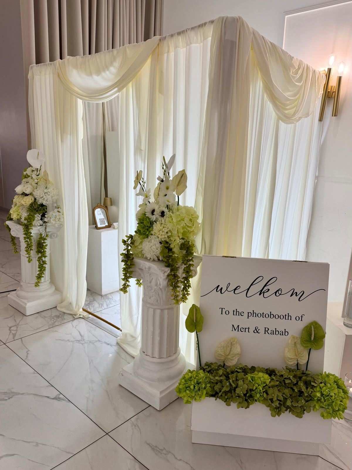 Photobooth met crème draperie, bloemzuilen en welkomstbord