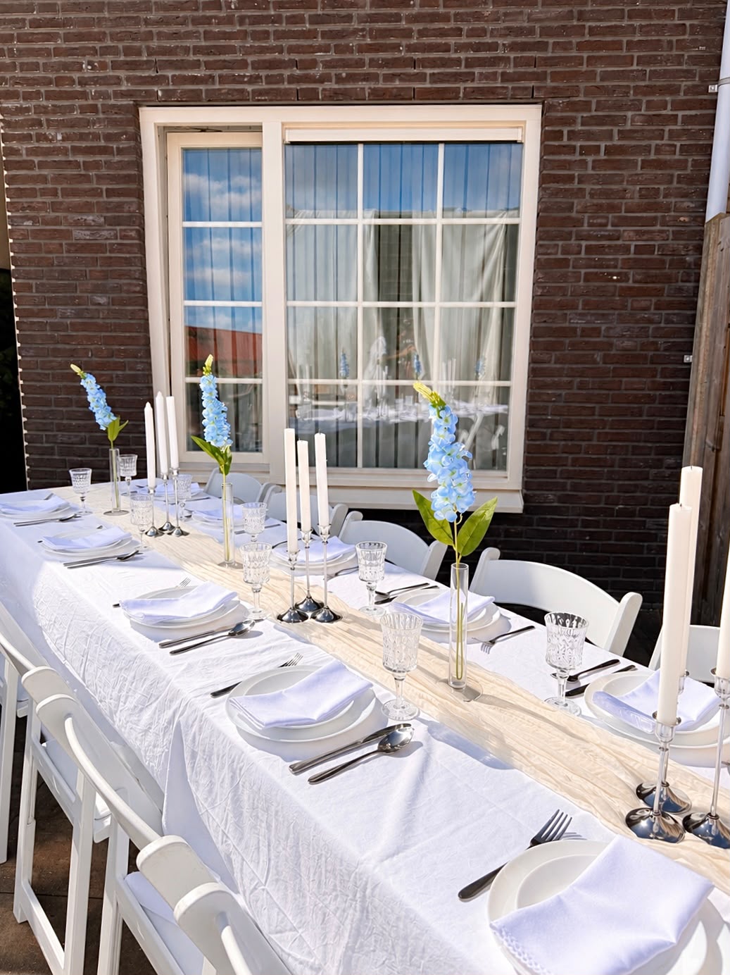 Lange tafel buiten met witte linnen, crème loper en blauwe delphinium