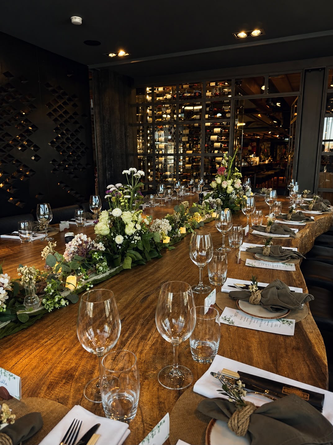 Lange houten tafel in restaurant met bloemenloper en groene servetten