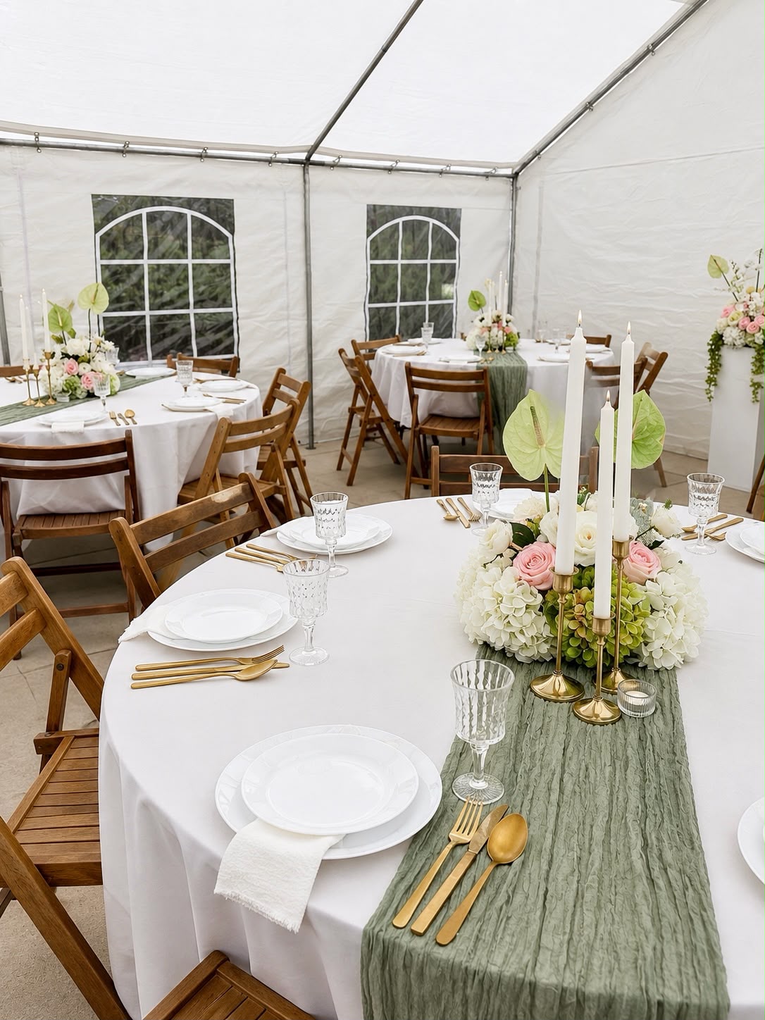 Ronde tafels in een tent met saliegroene lopers, gouden bestek en bloemstukken
