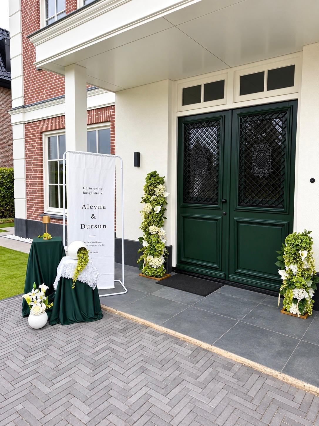 Welkomstbanner bij de voordeur met groene bloemzuilen en donkergroene tafelkleden