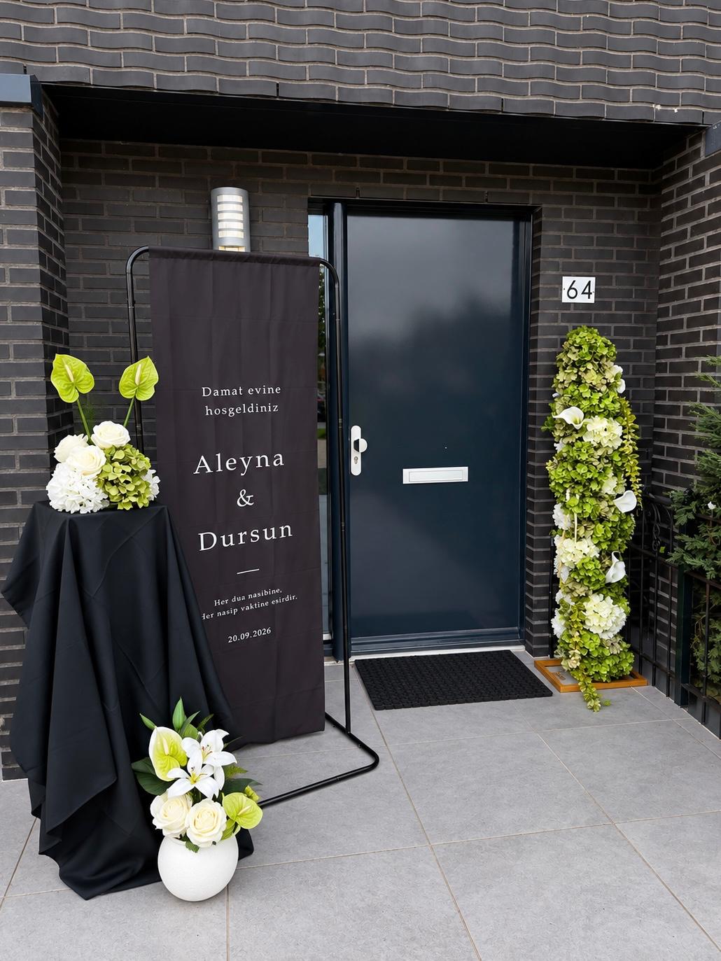 Zwarte welkomstbanner bij de voordeur met bloemzuil en witte bloemen